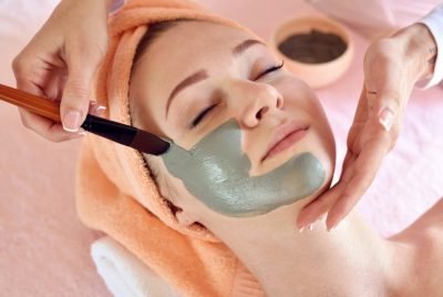 Face peeling mask, spa beauty treatment, skincare. Woman getting facial care by beautician at spa salon, side view, close-up